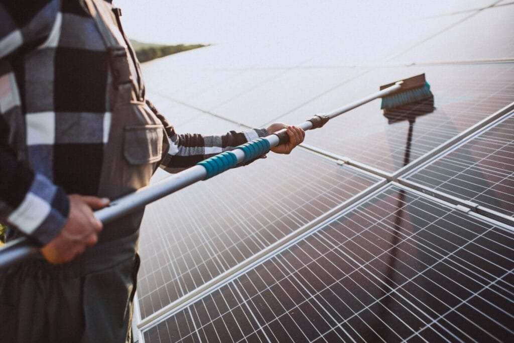 Cleaning solar panels with a long-handled brush or a pressure washer.